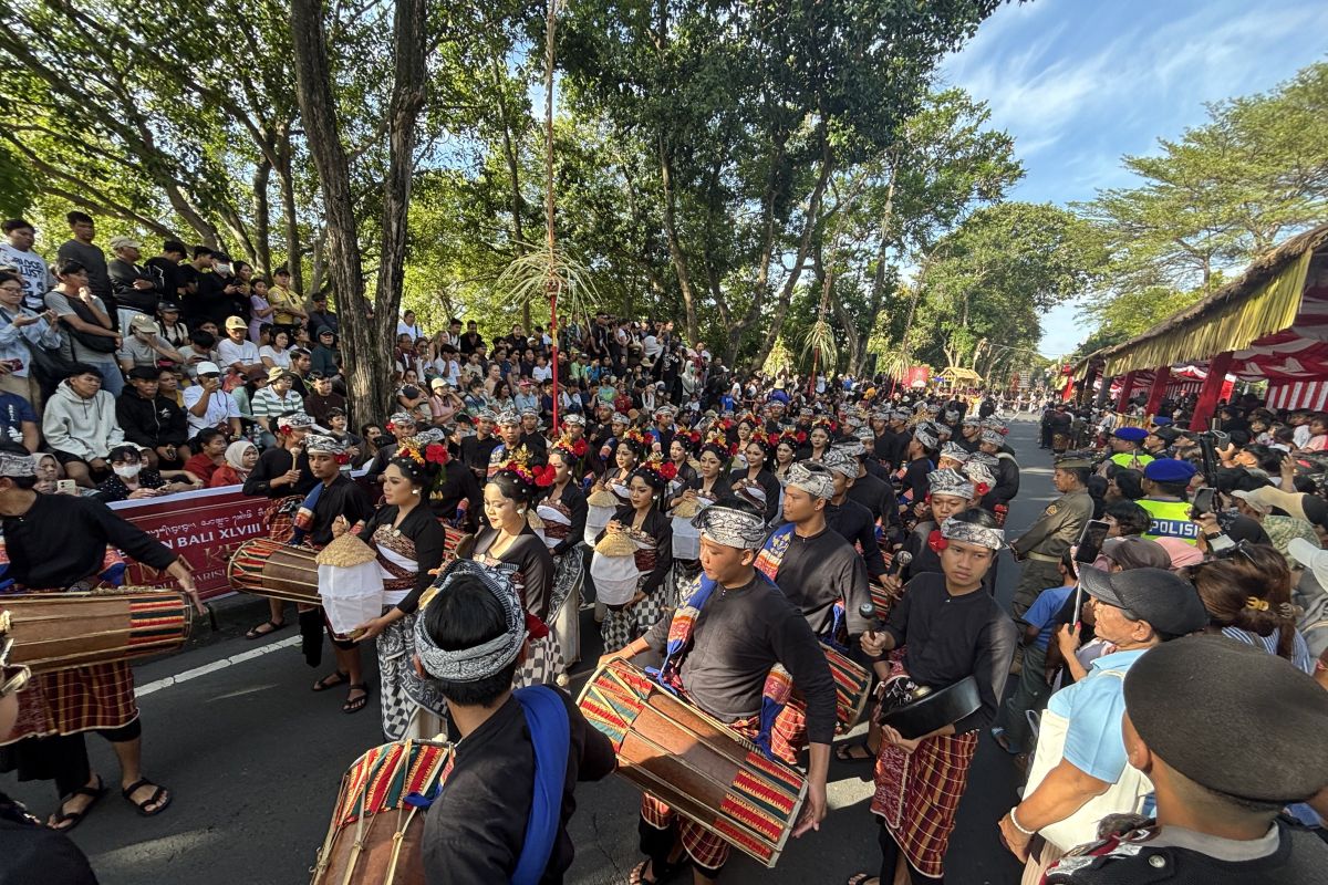 Foto ribuan pengunjung dan wisatawan yang memadati area jalan raya di depan Monumen Perjuangan Rakyat Bali Renon saat pawai pembukaan Pesta Kesenian Bali dengan latar belakang seniman memakai kostum tradisional berwarna emas dan merah.